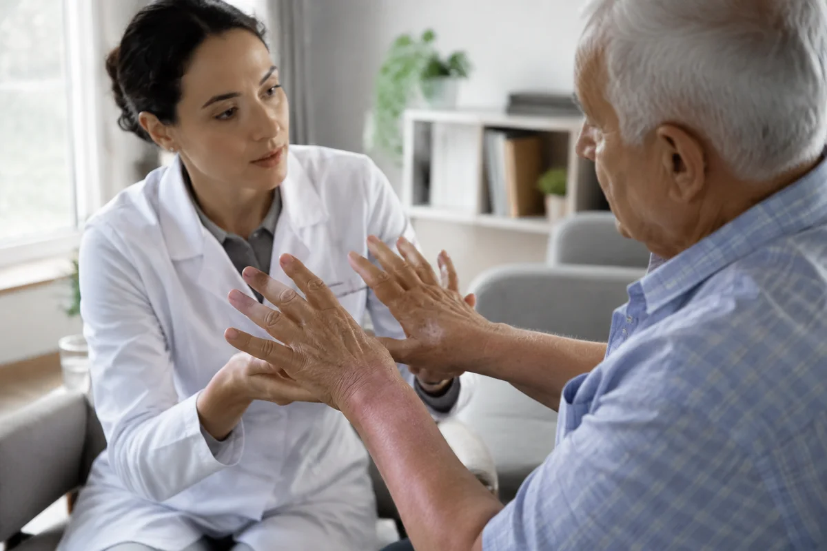 Imagem ilustrativa: Especialista avalia mãos de idoso com tremor em consulta de neurologia funcional.